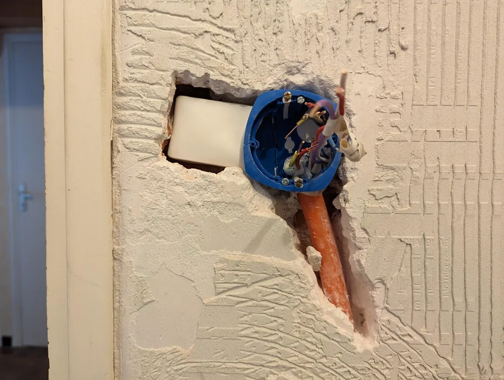 Boîte d'encastrement ouverte dans un mur en cours de travaux, avec les fils électriques